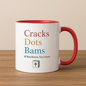 May include: White ceramic mug with a red interior and handle. The mug features the words "Cracks Dots Bams" in red, gold, and blue, with the text "If You Know, You know" below. A green tile with a symbol is also on the mug.