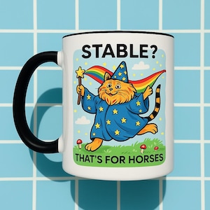 May include: White ceramic mug with a black handle and rim. The mug features a cartoon cat dressed as a wizard, holding a star wand and a rainbow flag. Text on the mug reads "STABLE? THAT'S FOR HORSES."