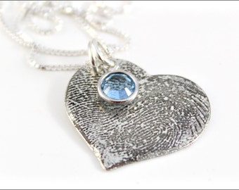 May include: A silver heart-shaped pendant necklace with a fingerprint design and a light blue gemstone in the center.
