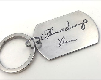 Könnte beinhalten: Ein silberner Schlüsselanhänger mit einem Hundemarkenanhänger, auf dem eine handschriftliche Unterschrift steht, die "Your always, Shana" lautet.