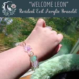 May include: An acrylic bracelet featuring translucent charms in pastel shades of pink, green, and purple, connected by gold-toned metal jump rings. The charms include star and circular shapes with spiral patterns, creating a layered, colorful accessory.