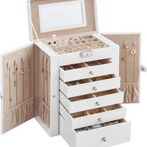 May include: A white jewelry box with multiple drawers and compartments. The box is open, revealing various pieces of jewelry, including necklaces, earrings, and rings. The interior is lined with a beige fabric, and a mirror is visible on the inside of the lid.