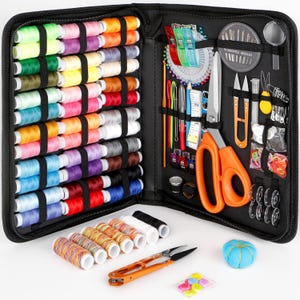 May include: A black zippered sewing kit, open to reveal a variety of sewing supplies. The kit includes spools of colorful thread, needles, scissors, measuring tape, and other tools. Additional items include a blue pincushion, small colorful buttons, and orange handled scissors.