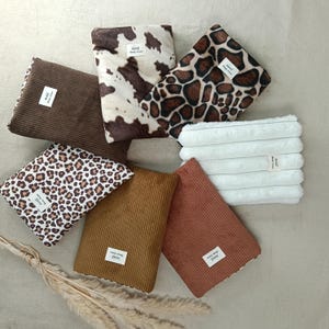 Peut inclure: Une collection de sept pochettes rectangulaires aux textures et motifs variés, incluant du velours côtelé marron, un imprimé vache blanc et marron, un imprimé léopard, du velours côtelé beige et rouille, et de la fausse fourrure blanche.