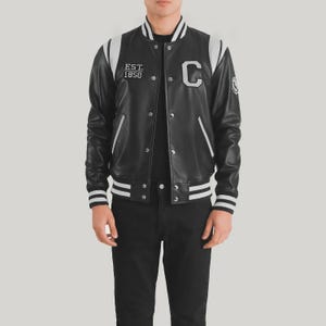 May include: Black varsity jacket with white accents on the shoulders, collar, and cuffs. Features the letter "C" and the text "EST. 1850" on the chest. The jacket has a button-up front and a classic athletic style.