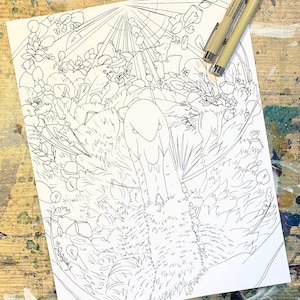 May include: A black and white line drawing of a swan surrounded by foliage, flowers, and rays of light. Two fine-tipped pens rest on the paper. The artwork is on a white sheet of paper, placed on a wooden surface.