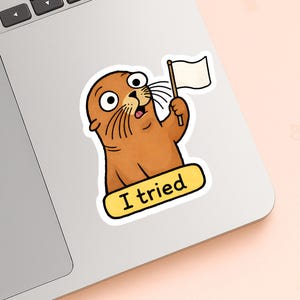 May include: A sticker of a cartoon seal with brown fur, large eyes, and a surprised expression. The seal holds a white flag and a yellow banner with the text "I tried". The sticker is on a laptop.