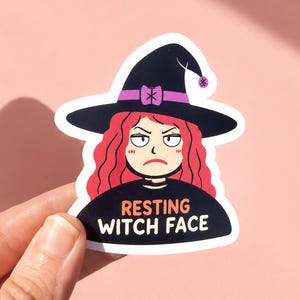 May include: A die-cut sticker featuring a cartoon character with wavy red hair wearing a black witch hat with a purple band and a black shirt. The character has a grumpy expression and the text RESTING WITCH FACE is printed in orange and white.