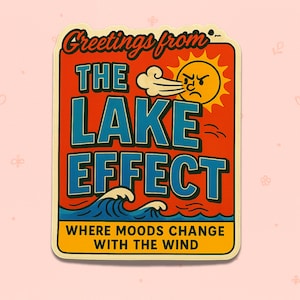May include: A rectangular sticker with a retro design. The sticker features the text "Greetings from THE LAKE EFFECT" in red and blue, with an illustration of a sun blowing wind. The bottom text reads "WHERE MOODS CHANGE WITH THE WIND".