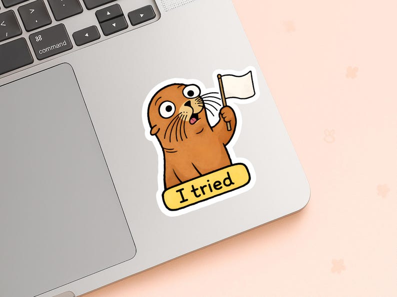 May include: A sticker of a cartoon seal with brown fur, large eyes, and a surprised expression. The seal holds a white flag and a yellow banner with the text "I tried". The sticker is on a laptop.