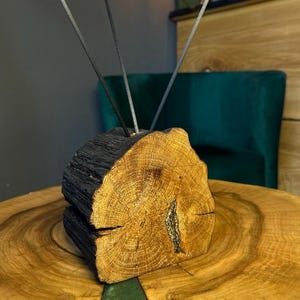 May include: A natural wood log incense holder featuring a charred black exterior and a light brown circular cross-section face with visible grain patterns and a central crack filled with metallic gold material, holding three thin grey incense sticks.