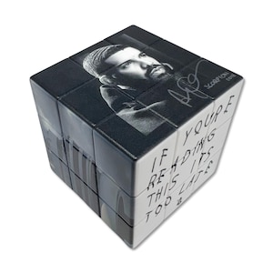 Op de afbeelding: Een Rubik's Cube met een zwart-wit portret van een man, zijn handtekening en het woord "Scorpion" op één kant. De tekst "IF YOU'RE READING THIS ITS TOO LATE" staat op een andere kant.