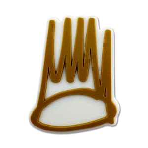 Könnte beinhalten: Ein weiß-goldener Schuhanhänger mit einem Kronen-Design. Die Krone hat einen goldenen Umriss und goldene vertikale Linien. Der Anhänger hat eine weiße Basis und besteht wahrscheinlich aus Gummi oder einem ähnlichen Material.