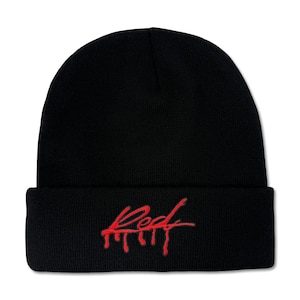 May include: Black beanie hat with the word "Red" embroidered in red script across the front. The word has a dripping effect, adding a unique design element to the hat. The hat is made of a soft, knitted material.