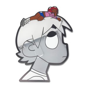 May include: A grayscale cartoon character head with a black outline and a small, colorful cartoon figure lying on top. The figure is wearing a pink shirt, blue shorts, and white shoes. The character has a large eye and a neutral expression.