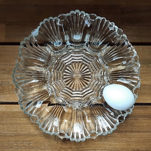 May include: A clear glass egg plate with a single white egg in one of the compartments. The plate has a scalloped edge and a starburst design in the center.
