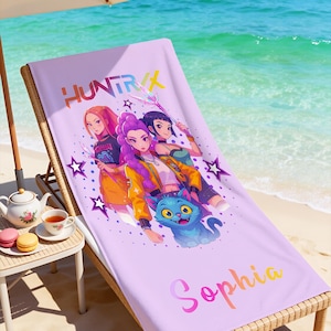 May include: A lavender beach towel with a colorful graphic of three anime-style figures and a blue cat. The towel has the text "HUNTR" and "Sophia" in a gradient font. The towel is on a wooden beach chair.