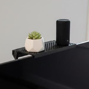 May include: A black monitor with a shelf holding a small succulent in a white geometric pot and a black cylindrical speaker. The monitor is on a white desk with a mouse and cable.