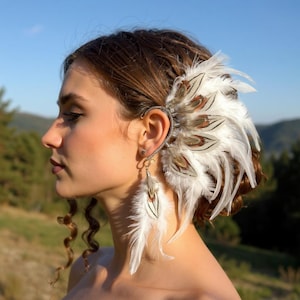 May include: An ear cuff and earring set featuring white and brown feathers. The ear cuff wraps around the ear with a decorative metal design. The earring dangles with a single feather.