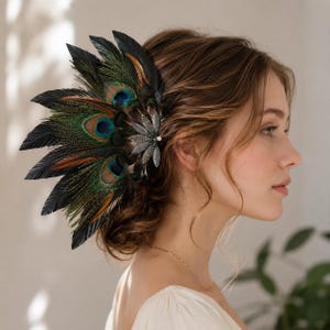 May include: A hair accessory featuring a fan of iridescent peacock feathers in shades of green, blue, and brown, accented with a silver-toned metal floral embellishment at the base, which is adorned with small clear crystals and a central white bead.