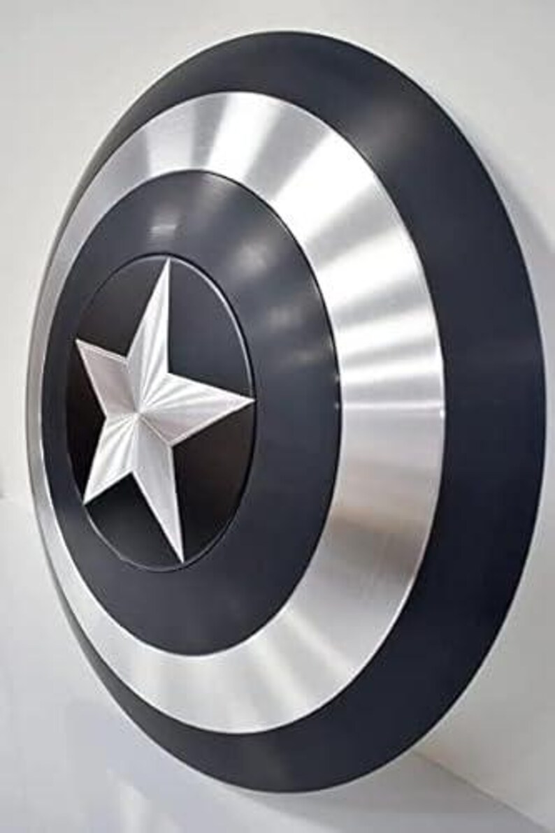 May include: A circular shield featuring a central silver star, encircled by bands of silver and black. The shield has a shiny surface and appears to be made of metal.