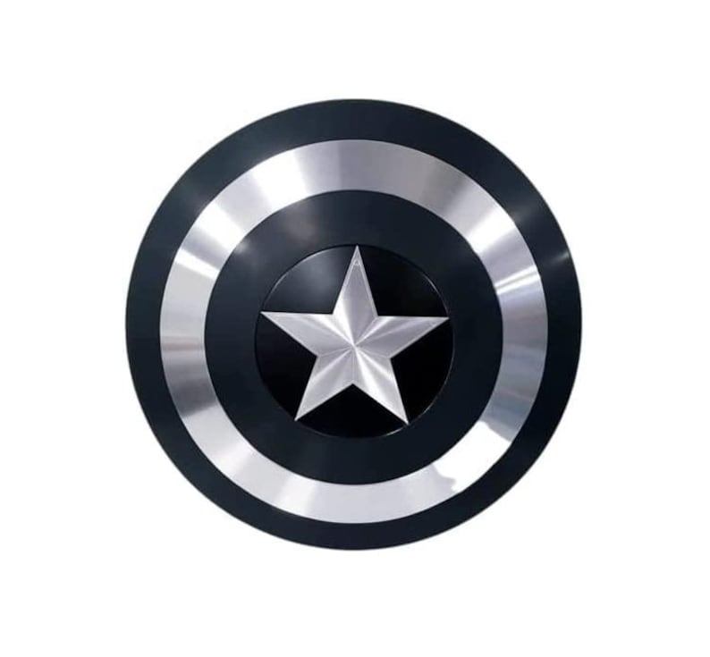 May include: A circular shield featuring a black border and a silver metallic inner ring. The centre of the shield is black with a silver, five-pointed star. The shield has a glossy finish against a white backdrop.
