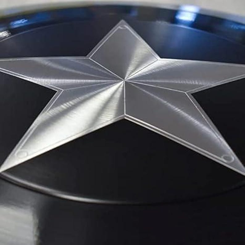 May include: A close-up of a black and silver shield. The shield features a large, five-pointed silver star in the centre against a black background. The star has a textured appearance, and the shield has a glossy finish.