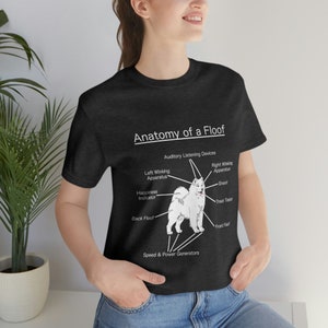 May include: A black t-shirt featuring a white illustration of a dog with the text "Anatomy of a Floof". The illustration shows the dog's body parts labelled with humorous names such as "Happiness Indicator", "Speed & Power Generators", and "Treat Tester".