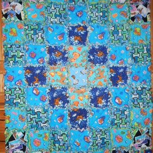 May include: A blue and brown patchwork quilt with a dog bone pattern. The quilt is made of various fabrics and has a frayed edge.