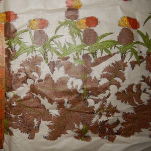 May include: A beige fabric with a repeating pattern of brown, green, orange, and yellow stylized thistle flowers. The fabric has a slightly textured surface.