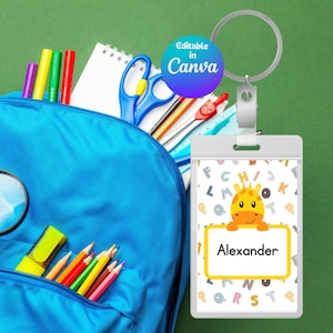 Peut inclure: Un sac à dos bleu rempli de fournitures scolaires dont une loupe, des crayons de couleur et des ciseaux. Un porte-badge rectangulaire avec un anneau métallique présente une girafe dessin animé et le nom Alexander sur fond blanc.