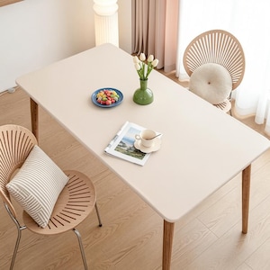 May include: A cream-coloured rectangular dining table with wooden legs, set with a blue plate of sweets, a green vase of tulips, and a cup of coffee. Two wooden chairs with cushions are positioned around the table.