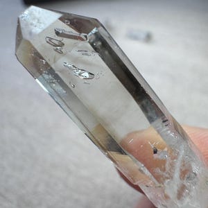 以下が含まれることがあります： 先端とファセットボディを備えた透明な水晶。結晶には内部インクルージョンがあり、人が持っているように見えます。結晶は透明で、わずかにスモーキーな色合いです。
