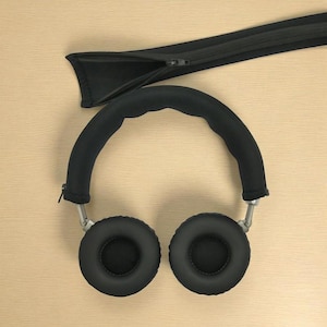 Può includere: Cuffie over-ear nere con cuscinetti e fascia imbottita. I bracci sono color argento. È presente anche una custodia nera con cerniera. Vista dall'alto.