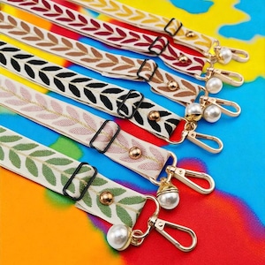 May include: A collection of colorful, embroidered bag straps with leaf patterns. The straps feature various colors, including yellow, burgundy, brown, black, pink, and green. Each strap has gold-colored hardware, including clasps and decorative pearl accents.