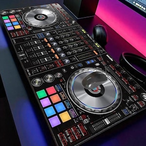 Op de afbeelding: Zwarte DJ-controller met zilverkleurige draaitafels, knoppen en schuifregelaars. De controller heeft kleurrijke vierkante pads en een muis. Het woord "serato" staat op de zijkant gedrukt. De controller staat op een bureau met een computermonitor op de achtergrond.