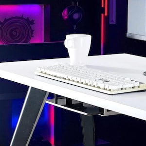 May include: A white computer desk with a white keyboard and a white mug. The desk has a metal frame and a shelf underneath. The background is dark with purple and red lighting.