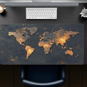 May include: A black desk mat featuring a world map design with gold and orange highlights. The mat is rectangular and covers a large portion of the desk. A white keyboard, mouse, and coffee cup are also visible.