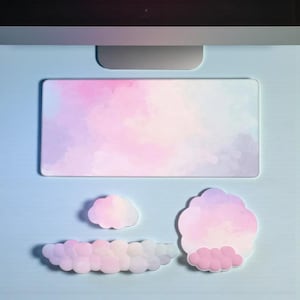 Puede incluir: Un tapete de escritorio y notas adhesivas con forma de nube en colores pastel. El tapete de escritorio rectangular presenta un diseño de acuarela en tonos rosa, morado y blanco. Las notas adhesivas tienen forma de nube, con una paleta de colores similar.