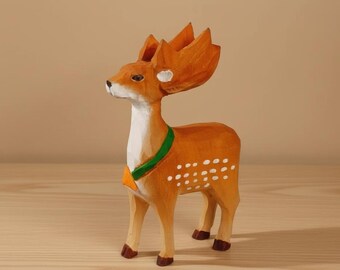 May include: A wooden deer figurine with an orange body, white spots, and a green collar. The deer has large, stylized antlers and is standing on a wooden surface. The figurine is hand-carved and painted, showcasing a rustic aesthetic.