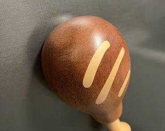May include: A wooden refrigerator magnet shaped like a roasted chicken leg. The magnet is brown with three light-colored stripes and a beige bone. The magnet is attached to a gray surface.