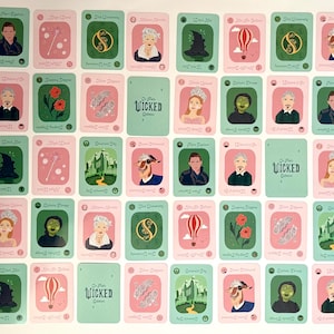 May include: A collection of playing cards with illustrations of characters and symbols from the musical "Wicked." The cards feature pink and green backgrounds with various images, including portraits, flowers, and a hot air balloon. The text "Wicked" is visible.