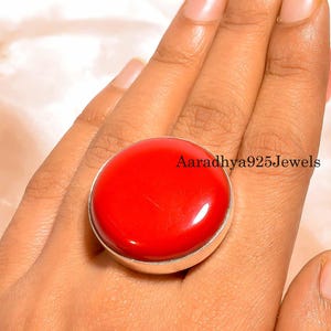 Könnte beinhalten: Ein großer, runder, roter Edelsteinring mit einem silbernen Band. Der Ring hat eine polierte, glänzende Oberfläche. Der Text "Aaradhya925Jewels" ist auf dem Ring zu sehen.