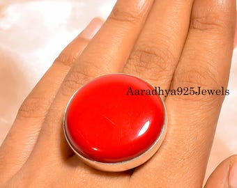 May include: A large, round, red gemstone ring with a silver band. The ring has a polished, glossy finish. The text "Aaradhya925Jewels" is visible on the ring.