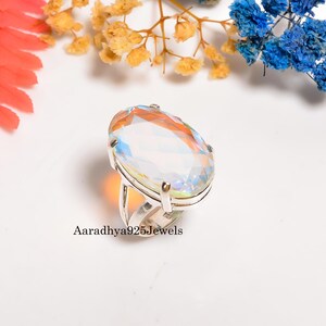 May include: A silver ring featuring a large, oval-cut gemstone with iridescent colors. The gemstone is set in a silver band. The text "Aaradhya925Jewels" is printed on the ring.
