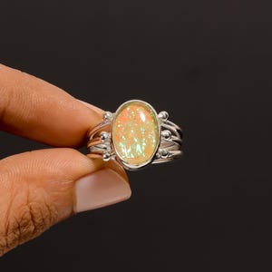 May include: A silver ring featuring an oval opal gemstone. The opal displays orange, yellow, and green hues. The ring has a multi-band design with small silver beads on the sides of the opal.