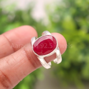 Puede incluir: Anillo de plata con una gema grande, ovalada y de color rojo intenso. El anillo tiene un diseño de caña dividida. El texto "Aaradhya 92.5 jewels" es visible.