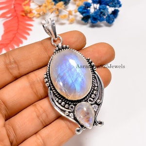 Puede incluir: Un colgante de plata con una gran piedra lunar ovalada e iridiscente y una piedra lunar más pequeña en forma de lágrima. El colgante tiene intrincados detalles metálicos y el texto "Aaradhya925Jewels".