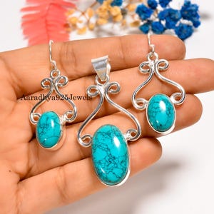 以下が含まれることがあります： ペンダントとイヤリングがセットになったシルバーのジュエリー。 各ピースは、装飾的なシルバーフレームにセットされた鮮やかなターコイズ色の楕円形の石を特徴としています。 ジュエリーセットは手の上に表示されます。