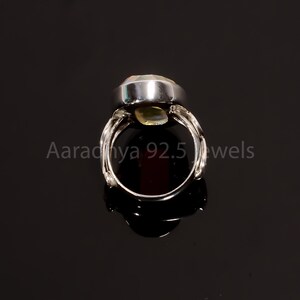 May include: A silver ring featuring a large, oval, pale-green gemstone. The ring has an intricate band design. The text "Aaradhya 92.5 jewels" is visible.